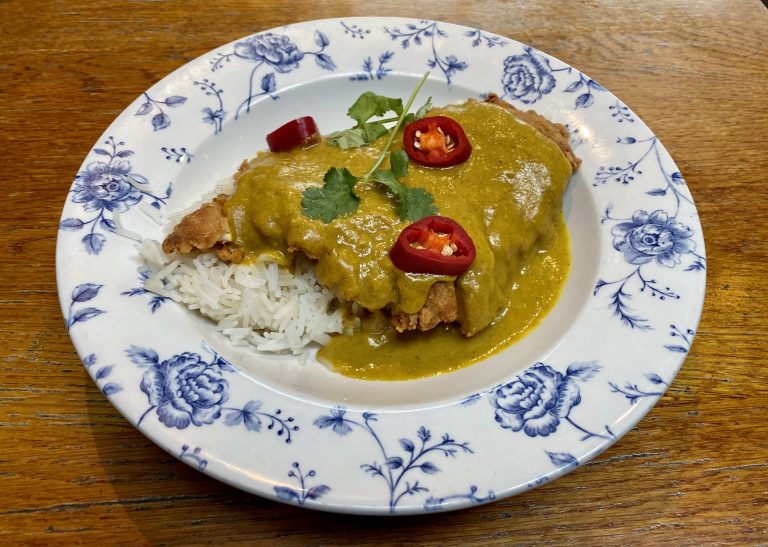 Katsu curry on plate, consisting of a layer of rice, chicken, and curry sauce.
