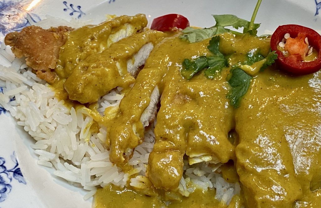 Close up shot showing layer of rice, slices of chicken cutlet, and a curry sauce layered on top.
