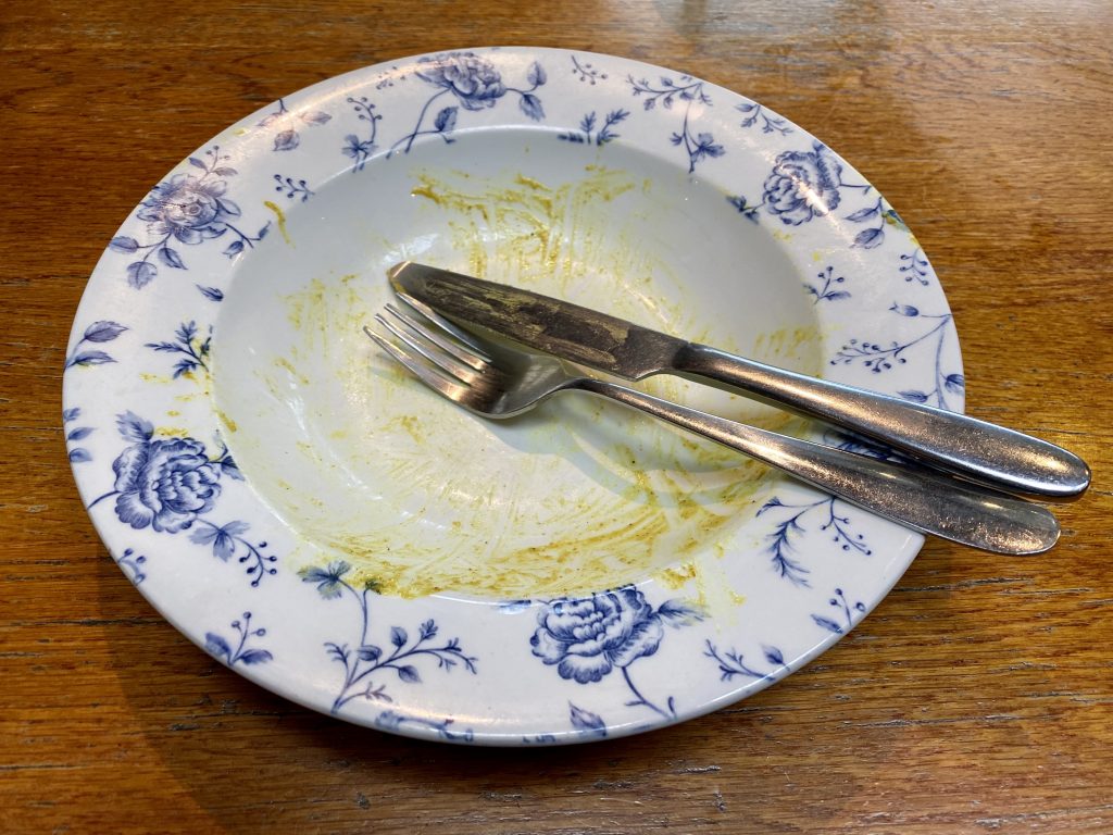 Clean plate on wooden table with knife and fork positioned to signify the customer has finished eating.