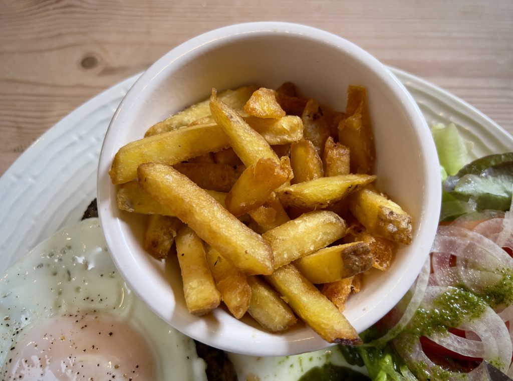 Homemade chips in a small white ramekin, on a plate with bistoque and salad.