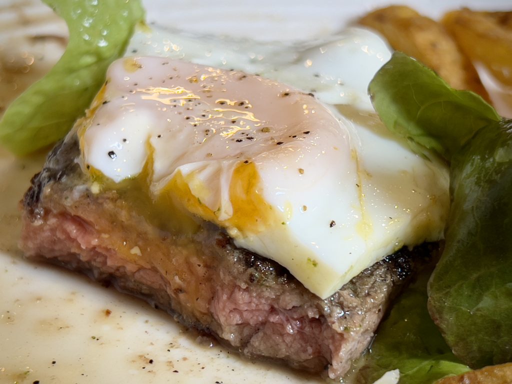 Cross-section of a bistoque steak and fried egg, showing the exposed pink meat and runny, orange yolk.