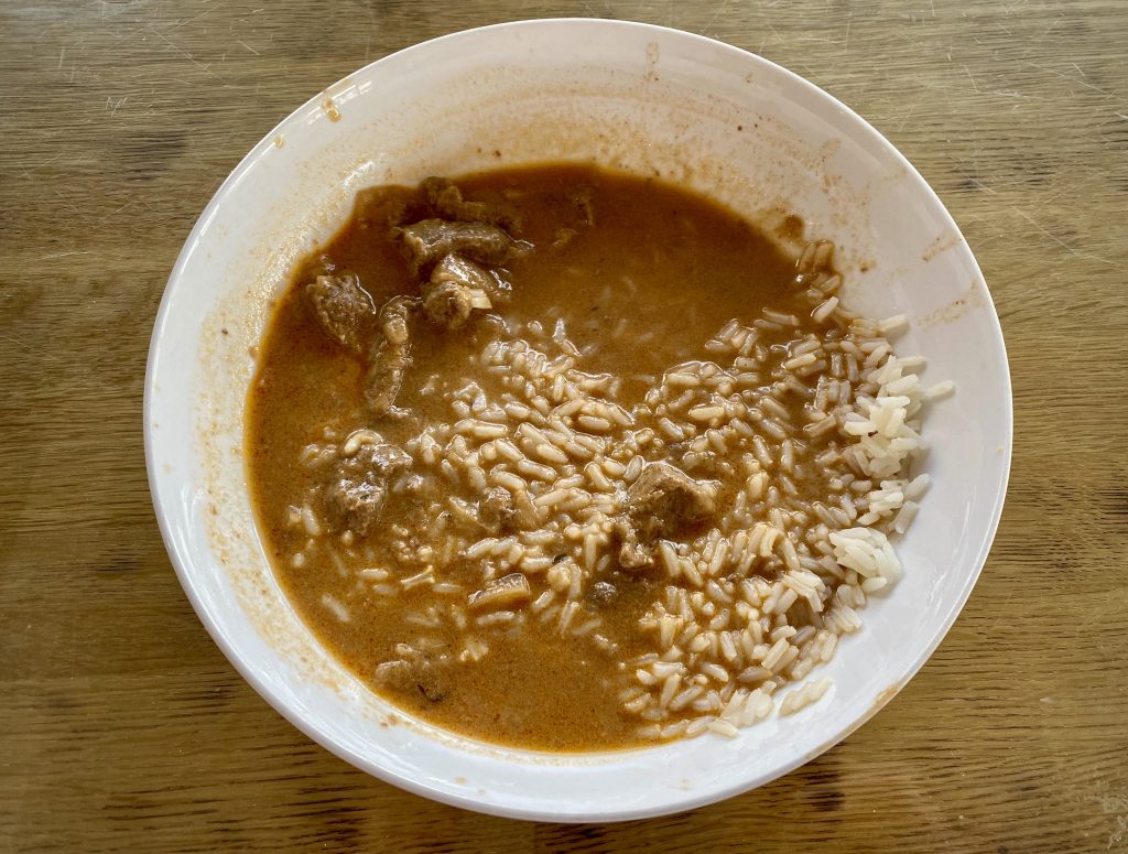 A half-eaten bowl of beef stroganoff and white basmati rice.