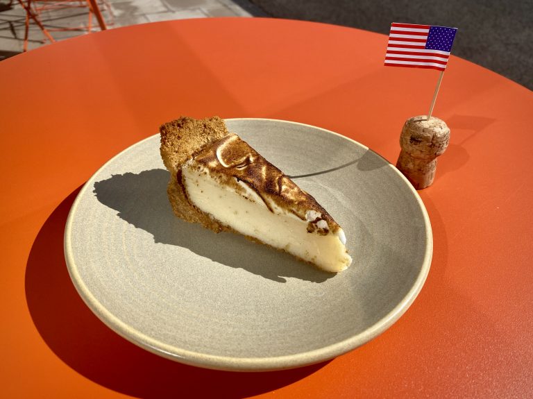 A slice of key lime pie on a grey plate, and a cork with an American flag cocktail stick in it.