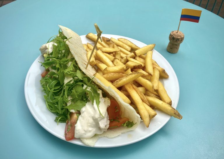 Chicken and aioli arepa with french fries on a white plate, next to a cocktail stick Colombian flag.