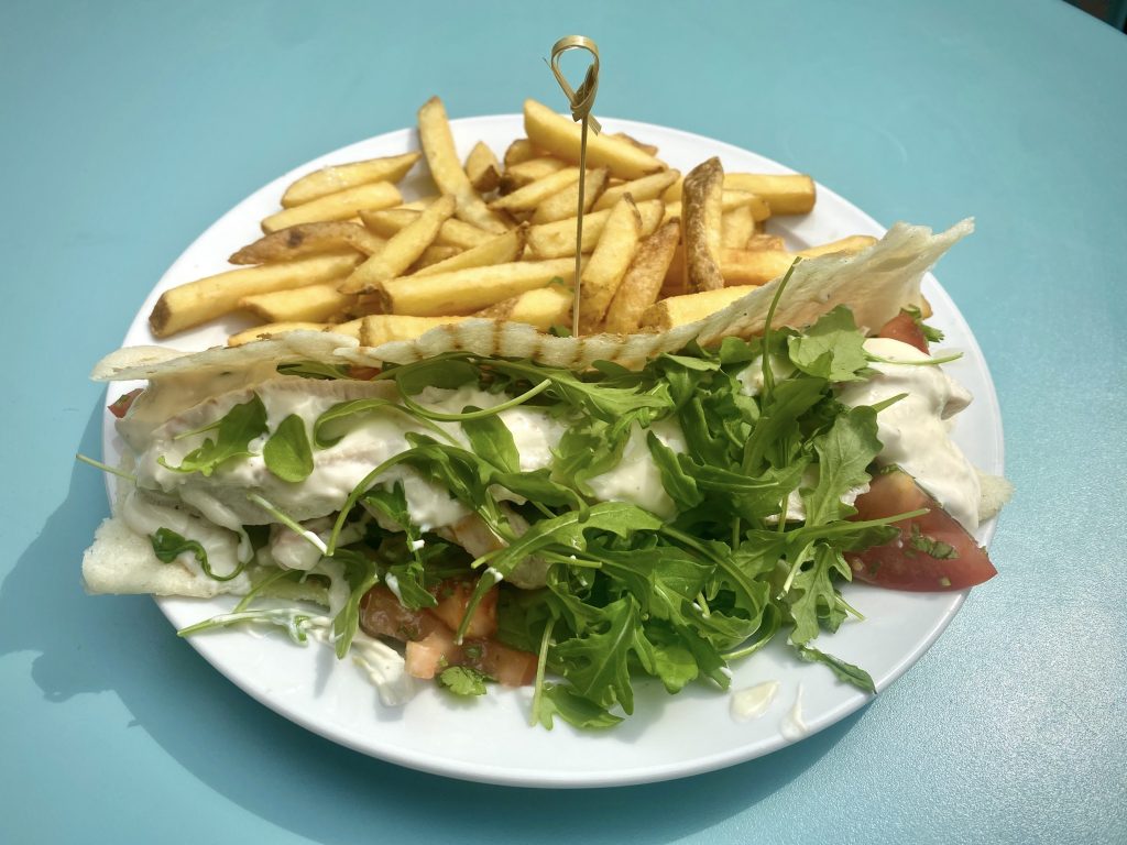 A white plate with a chicken and aioli arepa, along with a side of french fries.