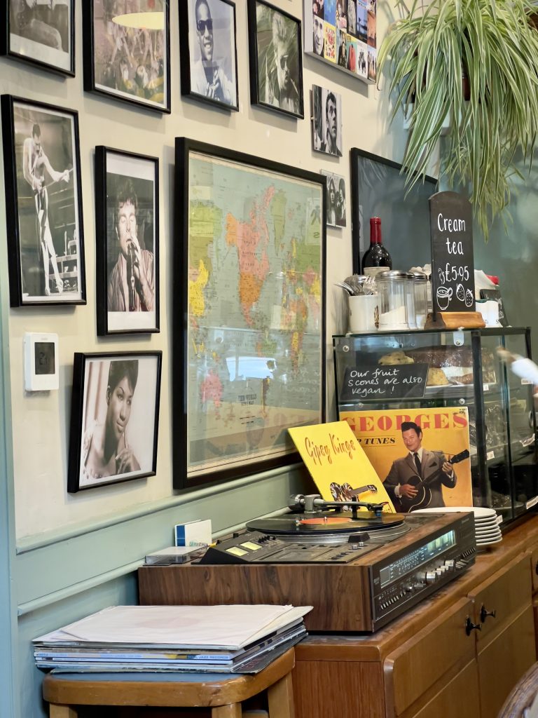 A record player on a wooden chest of drawers, next to a wall adorned with headshots of famous musicians.