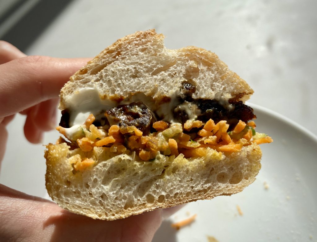 A cross-section of a banh mi, showing the bread, tofu, carrot shavings and mayonnaise.