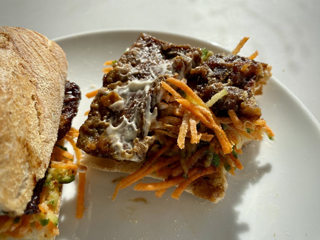 A disassembled banh mi, positioned to show its contents, with carrot shavings, tofu and mayonnaise visible.