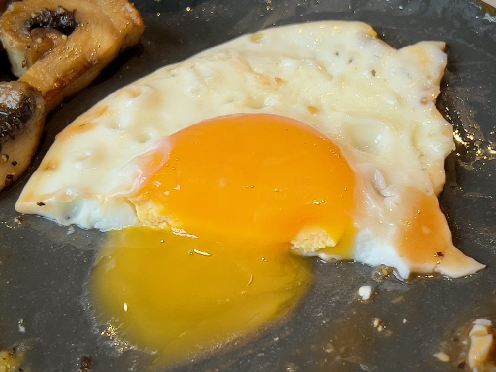 A fried egg cut in half, with the orange yolk running out on the plate.