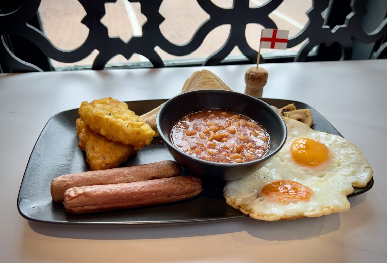 A Full English Breakfast, complete with sausage, eggs, hash browns, toast, beans and mushrooms, next to a English cocktail stick flag.