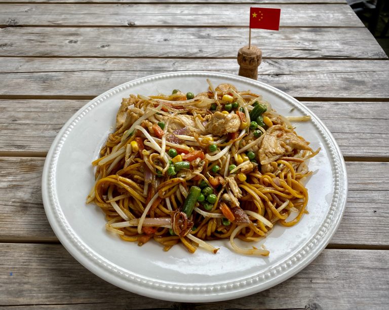 Chicken Chow Mein on a white plate, next to a Chinese flag cocktail stick.