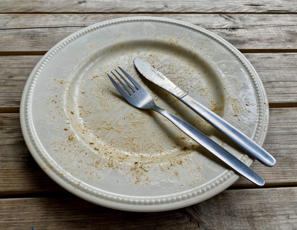 An empty white plate on a wooden table, with the knife and fork positioned to show one has finished eating.