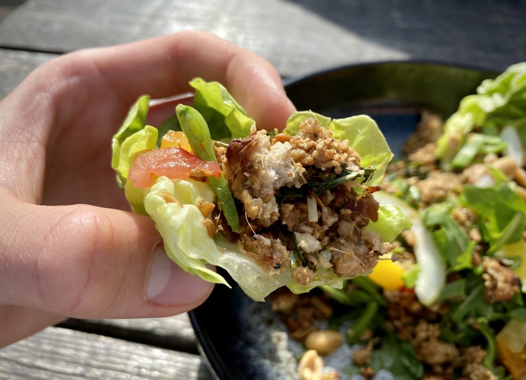 A hand picking up a baby gem lettuce cup of larb filling.