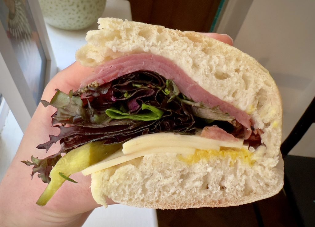 The cross-section of a New York Deli sandwich, showing the layers of mustard, cheese, mixed leaves and ham.