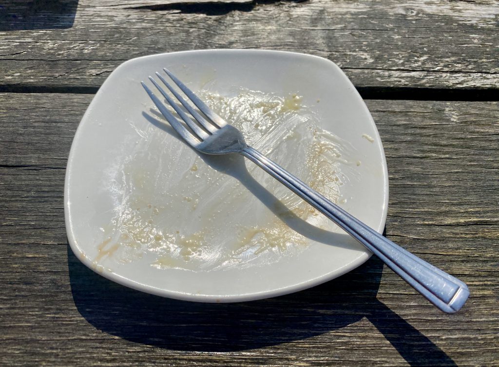 An empty white cake plate with a fork positioned to show that one has finished eating.