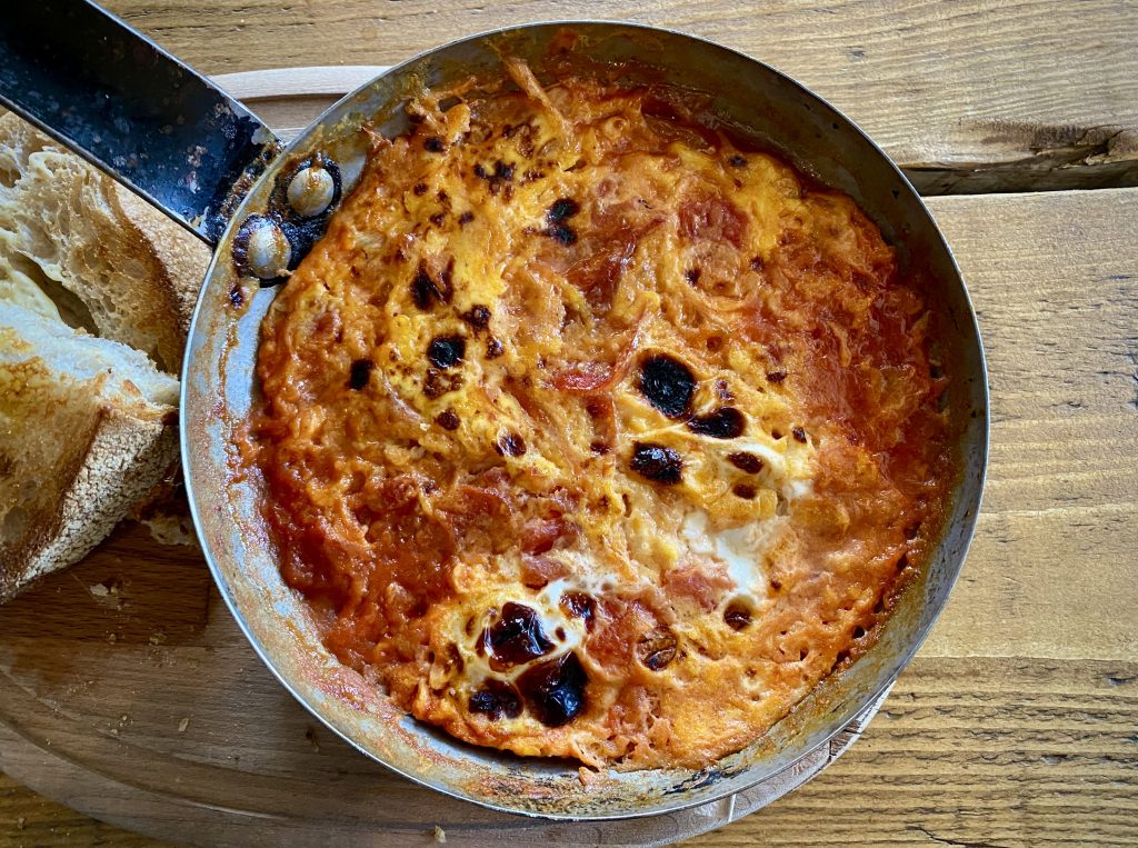 A top-down view of a Menemen in a small frying pan on a wooden table.