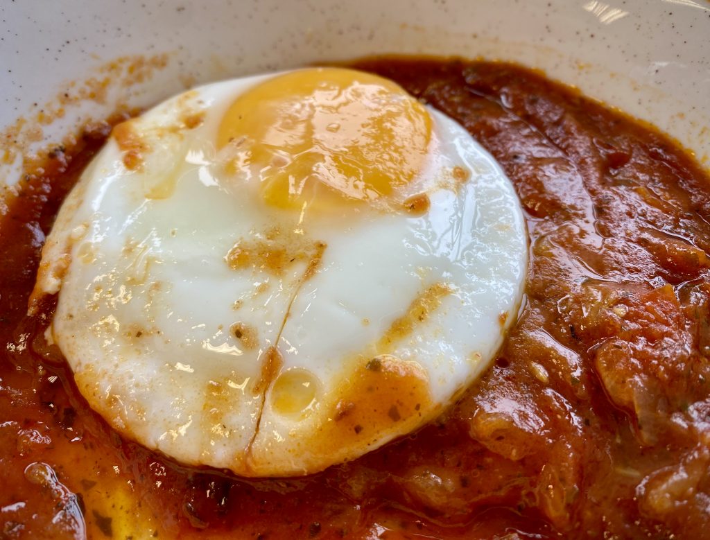 A close-up of a poached egg on top of a Shakshuka tomato sauce.