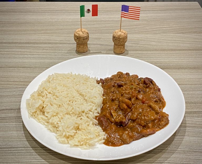 A Chilli con carne with rice on a white plate, next to Mexican and American cocktail stick flags.