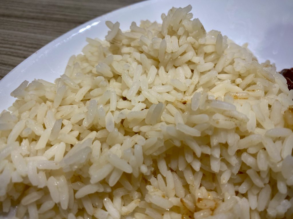 A close-up shot of long-grain white rice on a white plate.