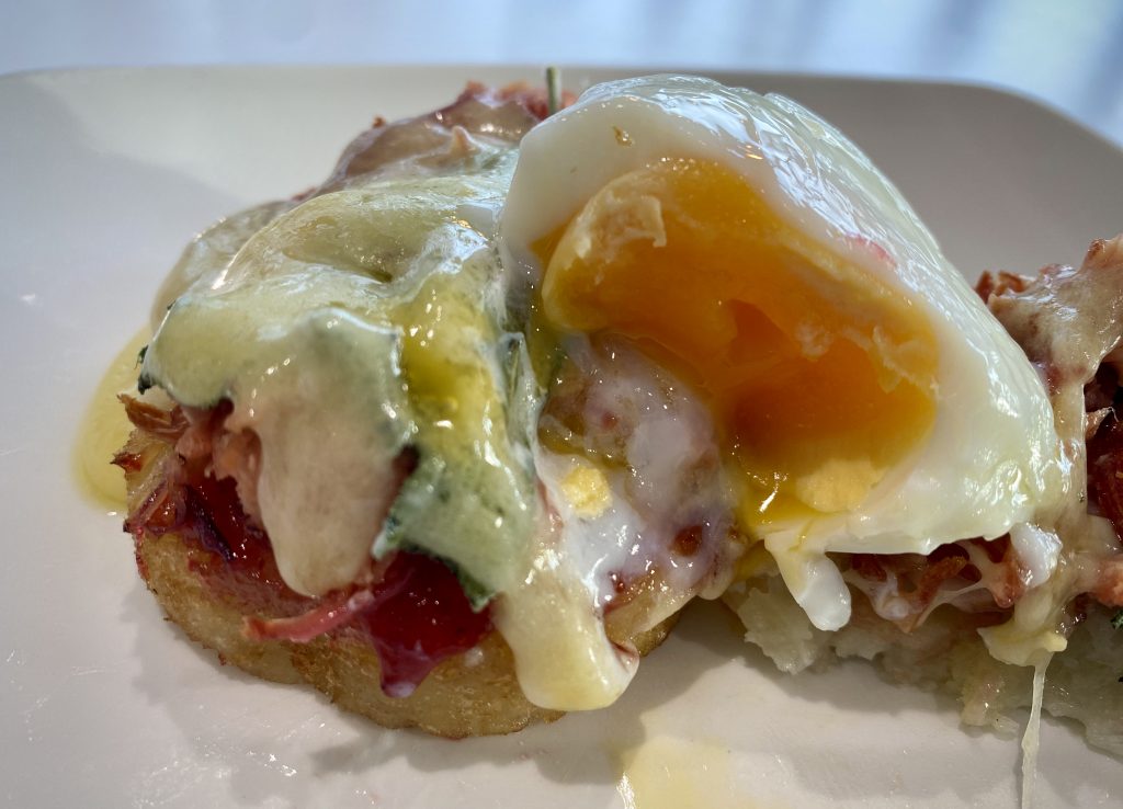 A close up of two potato röstis, adorned with ham hock, melted cheese, sage and a poached egg cut in half so its cross-section is visible.