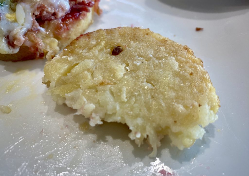 A close up of half a potato rösti on a white plate.