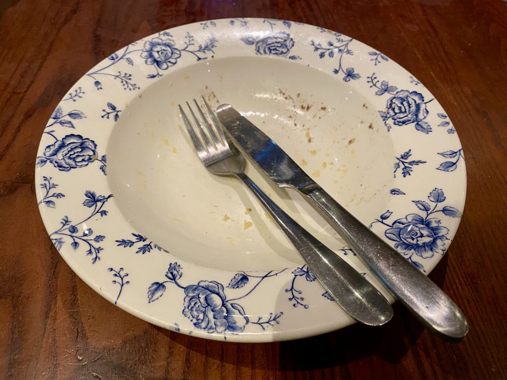 An empty plate with a knife and fork positioned across it, showing that one has finished eating.