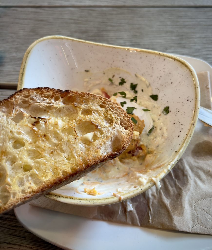 A near-empty plate of Cilbir (Turkish Eggs), with a slice of toasted and buttered sourdough in the foreground.