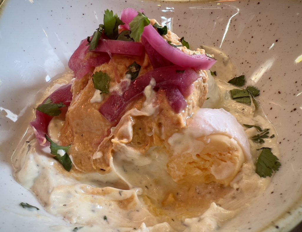 A cross-section shot of Cilbir (Turkish Eggs), showing the poached egg cut in half, pickled onions and hummus.