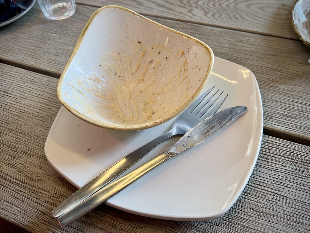 An empty white bowl on a white plate, with a knife and fork positioned across the plate to signal one has finished eating.